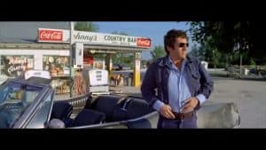 A man standing next to a car in front of a gas station.