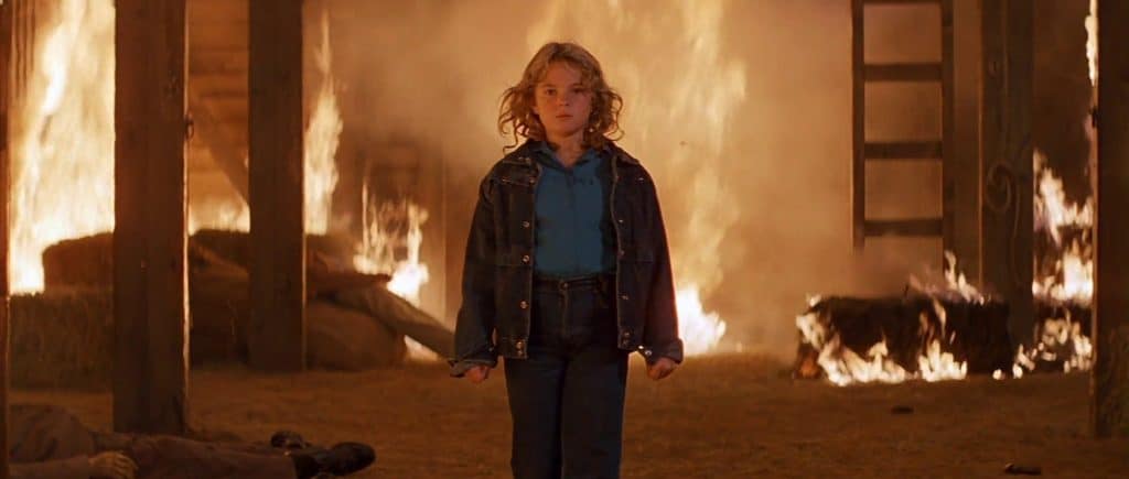 A boy standing in front of a fire in a barn.