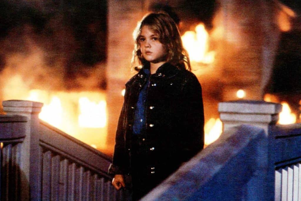 A young girl standing on a railing in front of a fire.