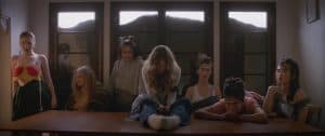 ‘Ladyworld’ Blu-Ray Review – The Delirium Of Isolation A group of people sitting around a table.