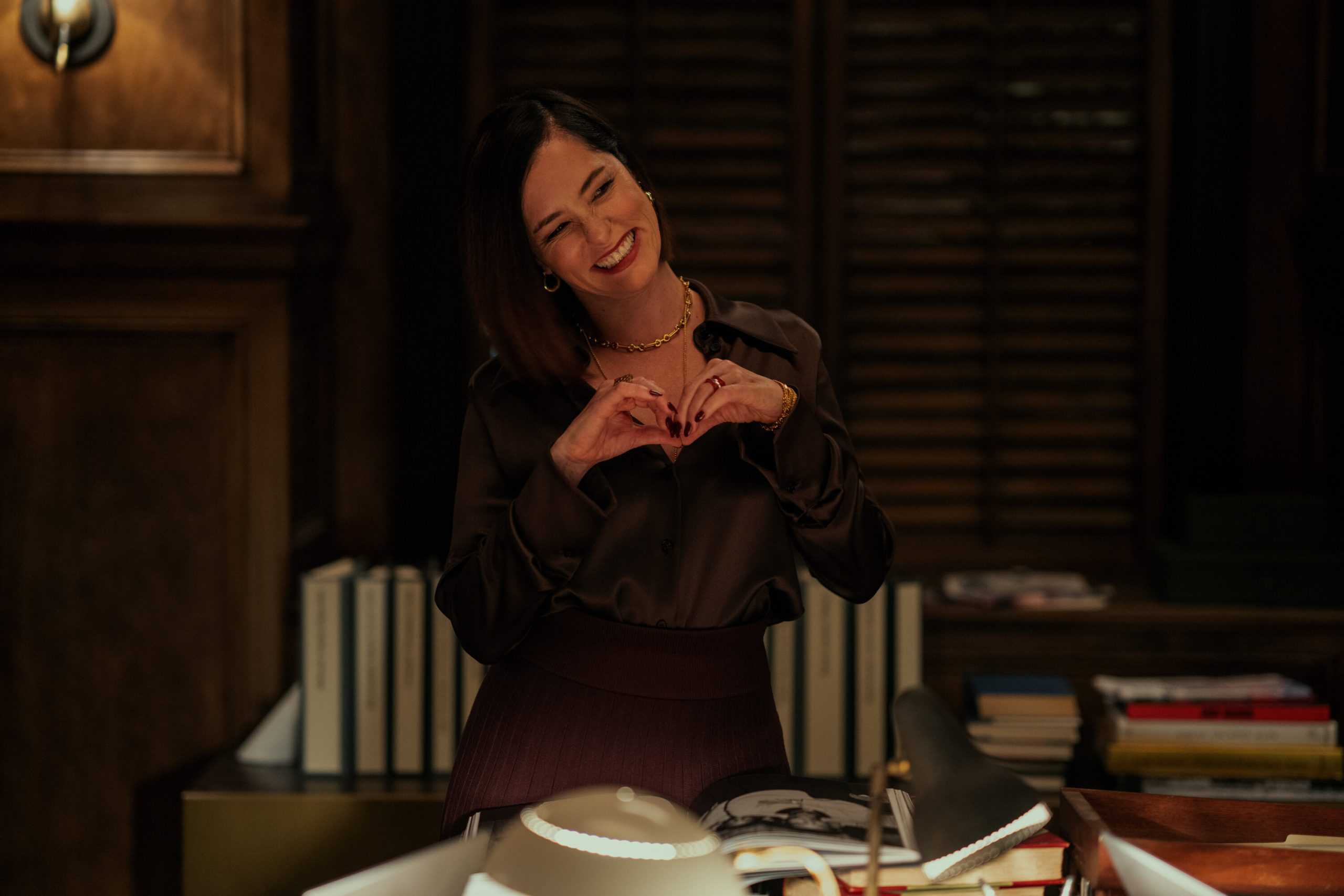 A woman making a heart shape in front of a desk.