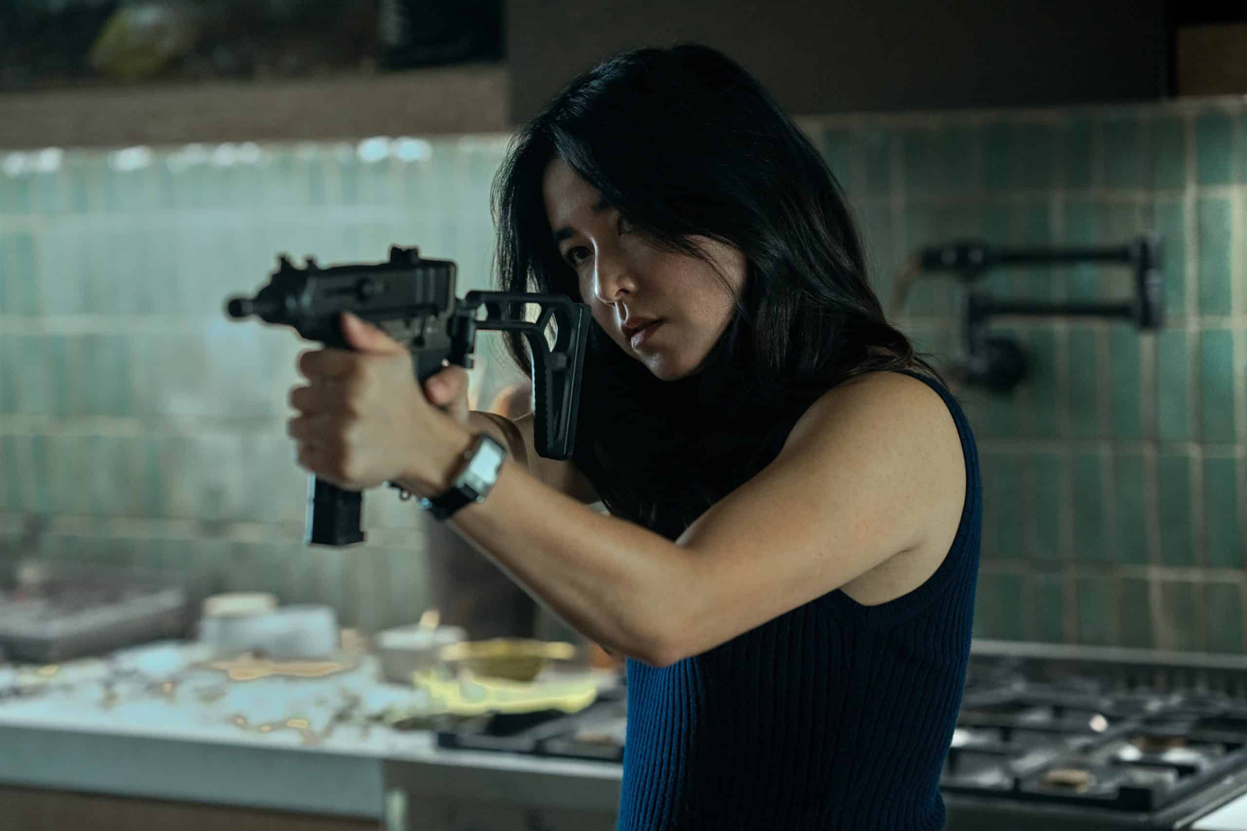 A woman holding a gun in a kitchen.
