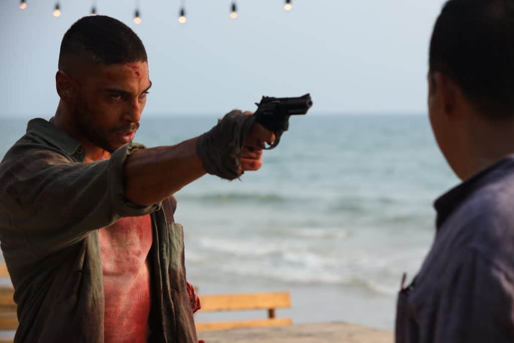 A man pointing a gun at another man on the beach.