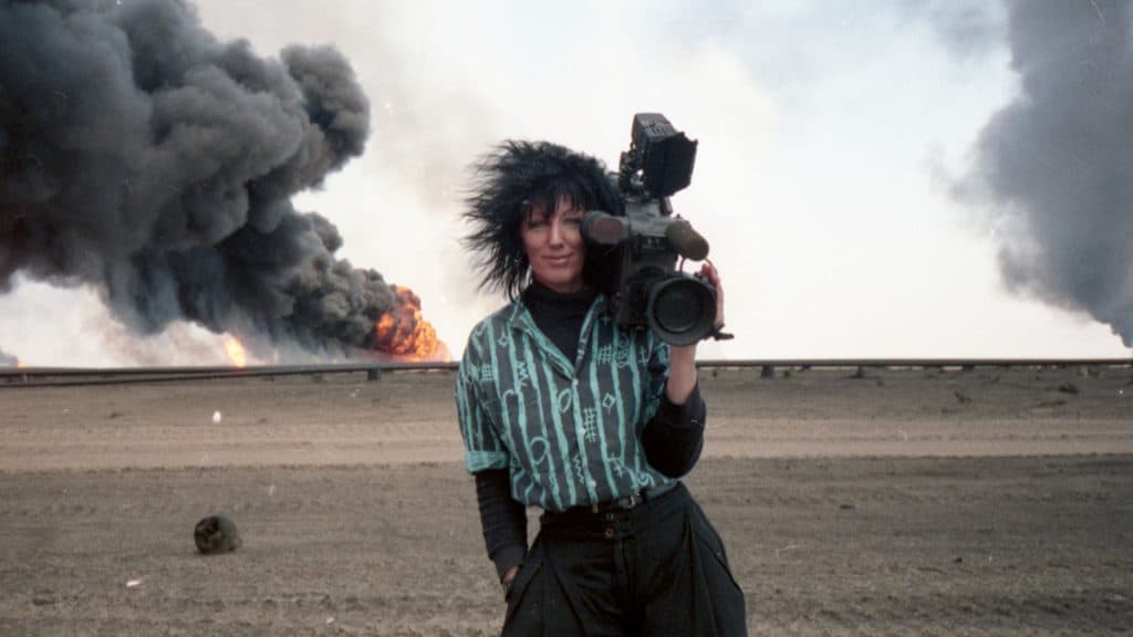 A man holding a camera in front of a fire.