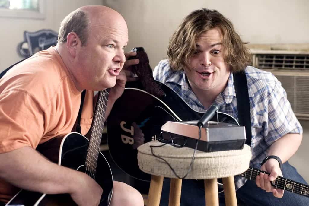 Two men sitting on a stool with guitars.