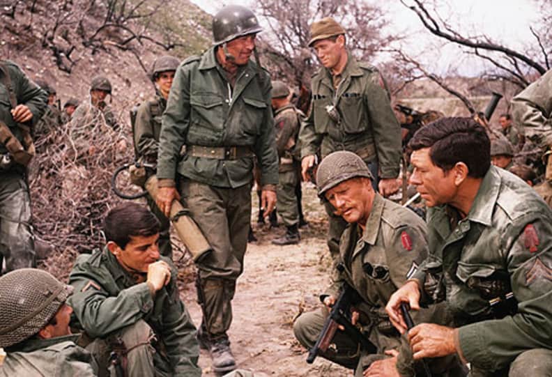 A group of men in military uniforms sitting on a dirt road.