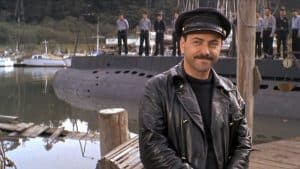 A man in a leather jacket standing next to a boat.