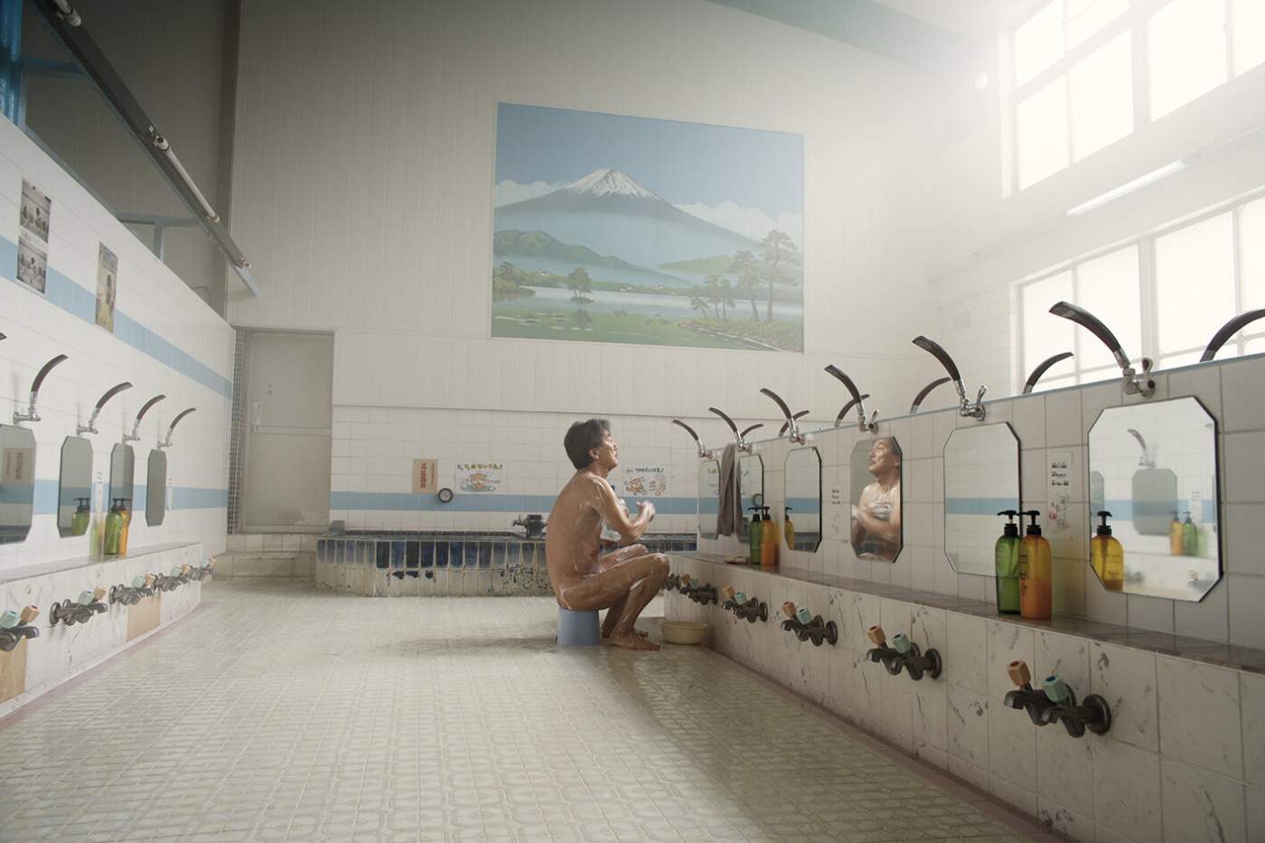 A man is sitting on a bench in a bathroom.