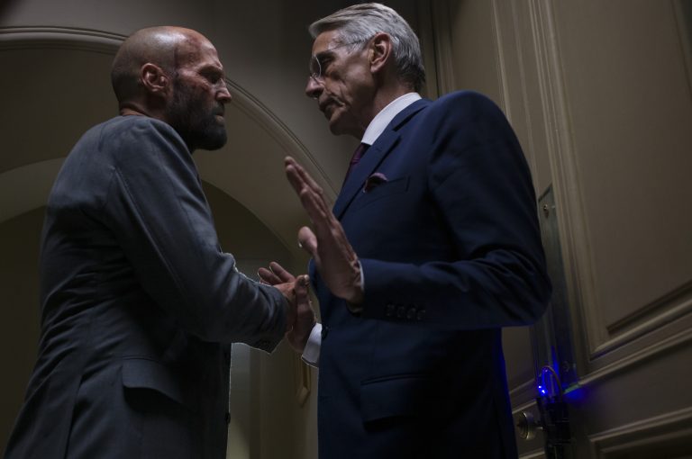 Two men in suits shaking hands in a hallway.