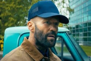 A bearded man in a blue hat is standing in front of a truck.
