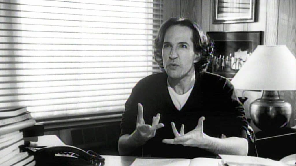 A man sitting at a desk with his hands up.