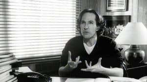 A man sitting at a desk with his hands up.