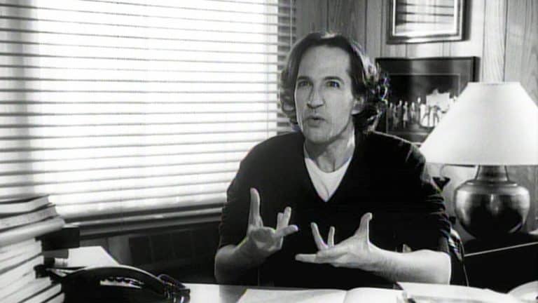 A man sitting at a desk with his hands up.