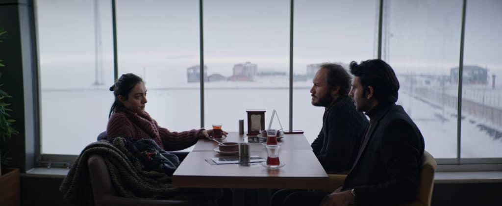 Three people sitting at a table in front of a window.