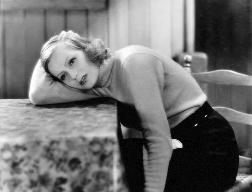 A woman leaning on a table with her hands on her hips.