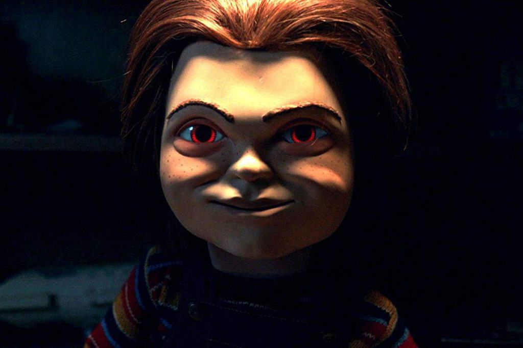 A doll with red eyes is standing in a dark room.