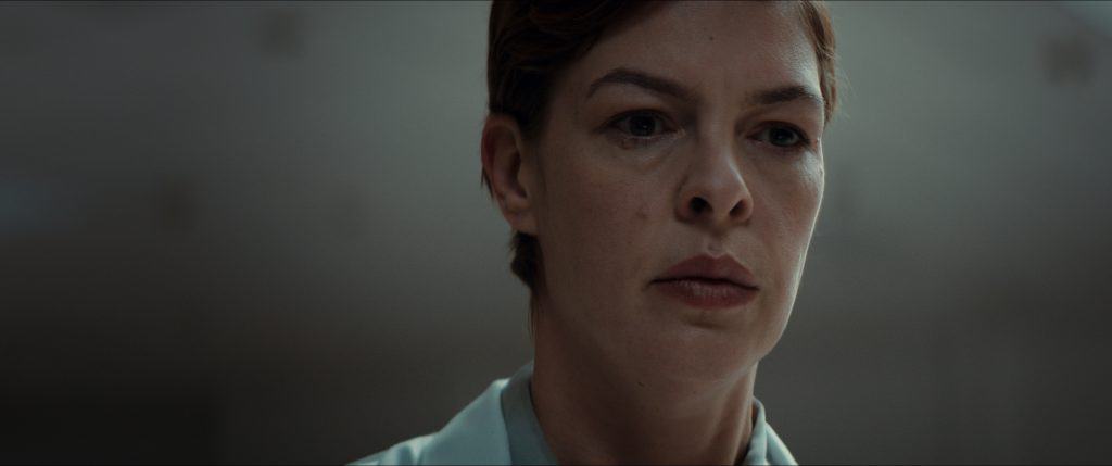 A woman in a white shirt is staring at the camera.