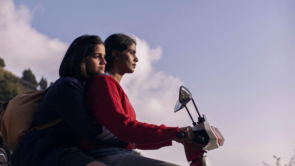 Two women are sitting on a motorcycle looking at the sky.