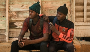 Two young men sitting on a bench with a cell phone.
