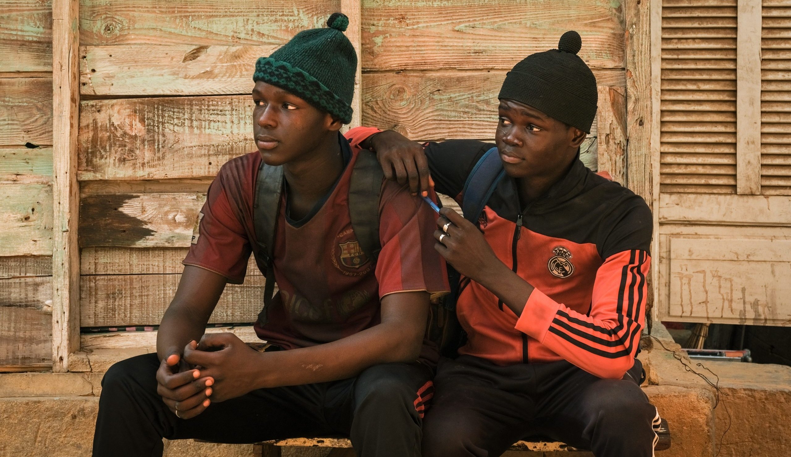 Two young men sitting on a bench with a cell phone.