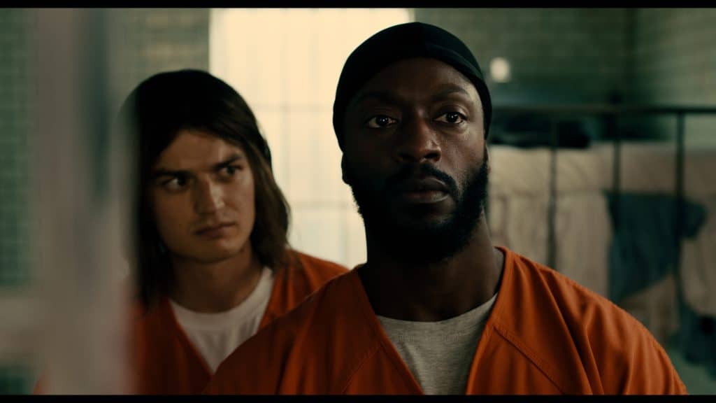 A man in orange jumpsuit looking at another man in orange jumpsuit.