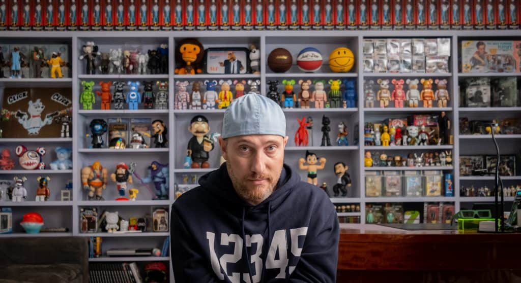 A man sitting in front of a shelf full of toys.