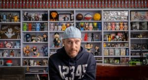 A man sitting in front of a shelf full of toys.