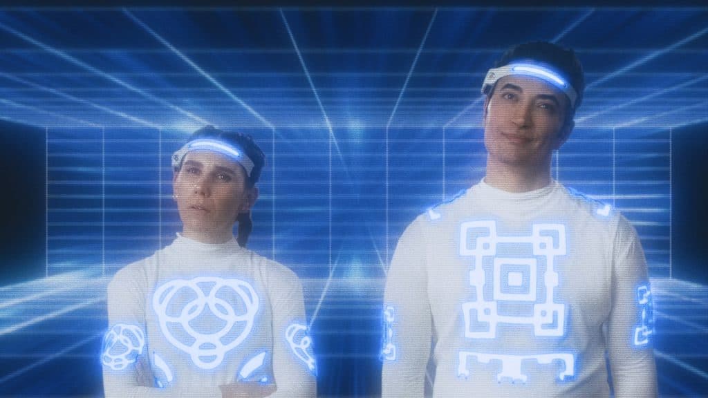Two people in a futuristic outfit standing in front of a blue background.