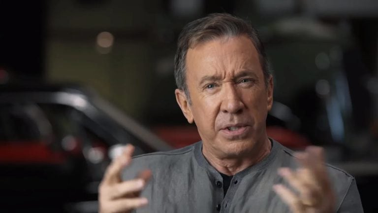 A man is talking in front of a car.