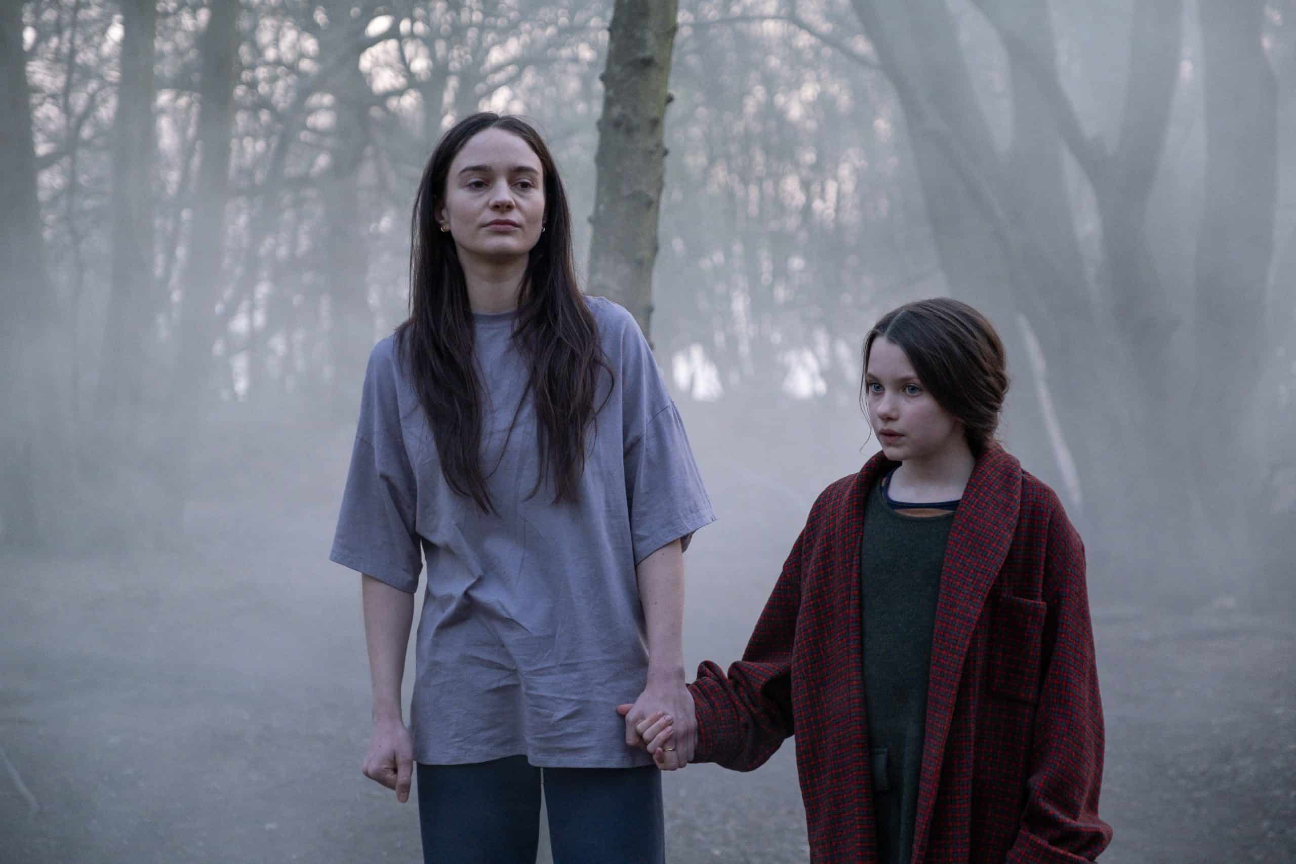 Two women holding hands in a foggy forest.