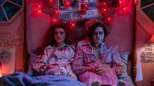 ‘Lisa Frankenstein’ Blu-Ray Review – Stylish Horror Comedy Succeeds In Spite Of Its Hiccups A man and woman in pajamas sitting on a bed with red lights.