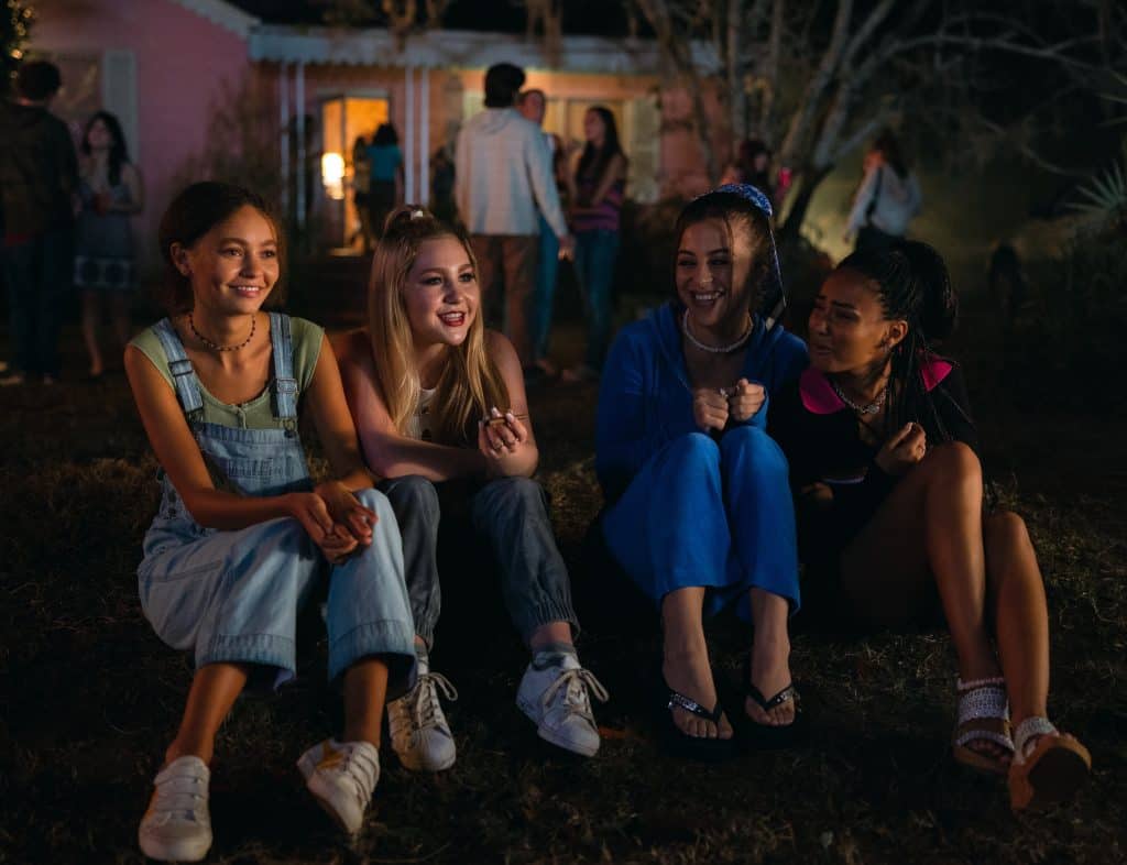 A group of girls sitting in front of a house at night.