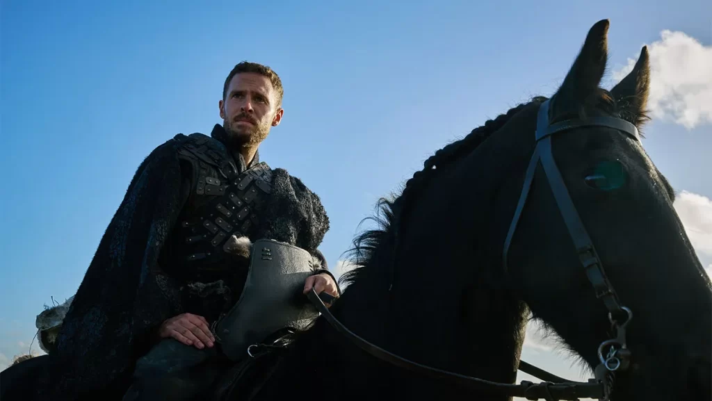 A man in a black cloak riding a horse.