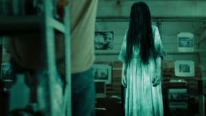 A woman in a white dress is standing in a dark room.