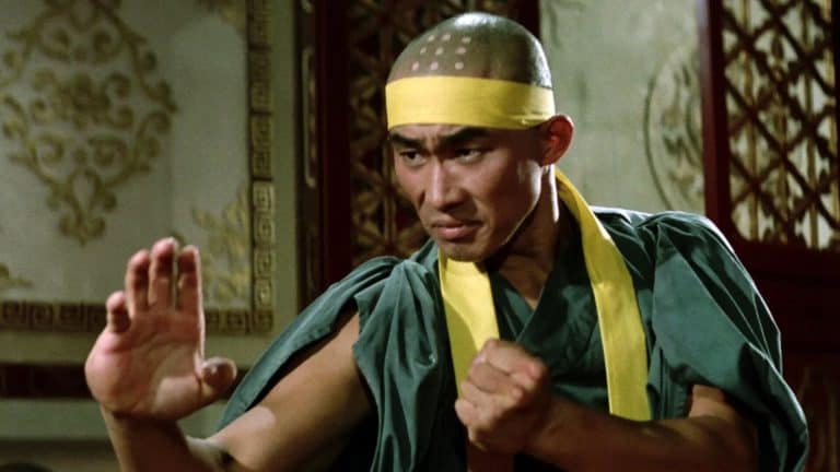 A man in a yellow robe is doing a martial arts move.