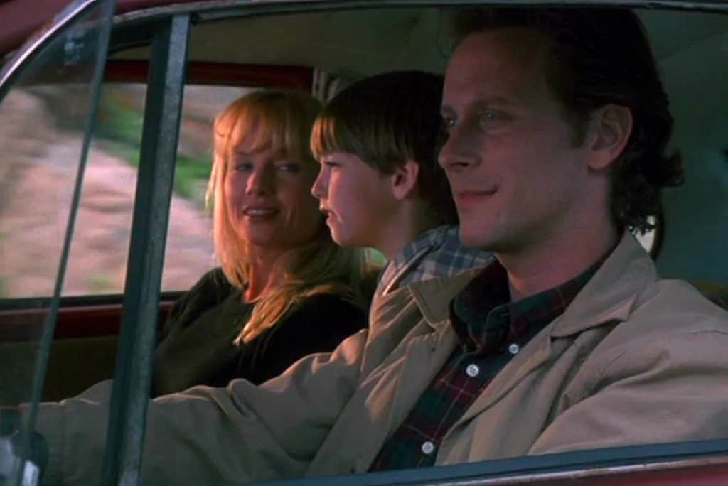 A man and woman in a red car with a child in the back seat.