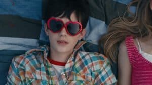 A boy and girl laying on a bed with heart shaped sunglasses.