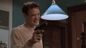 A young man holding a gun in front of a lamp.
