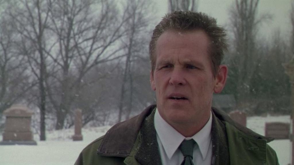 A man with a concerned expression standing in a snowy cemetery.
