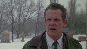A man with a concerned expression standing in a snowy cemetery.