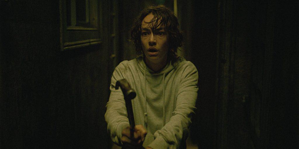 A young man holding a hammer in a dark hallway.