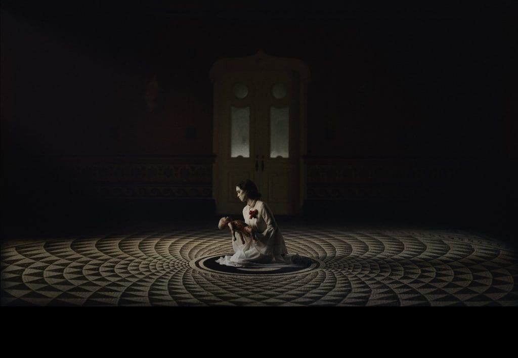A woman sitting on a circular floor in a dark room.