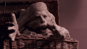 Alien creature prop with an oversized head and sharp teeth sitting in a wicker chair.