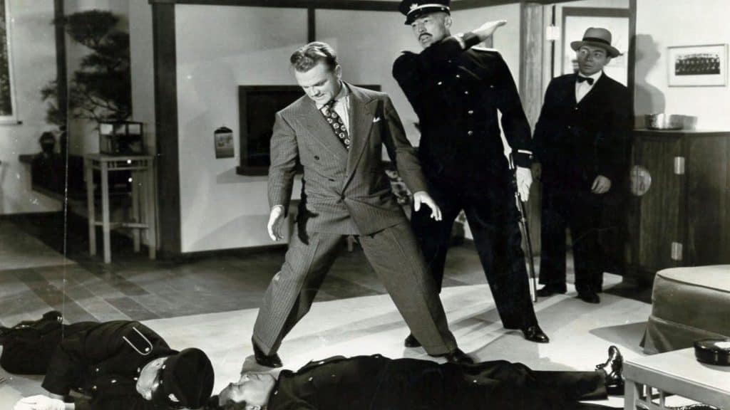 A man in a suit standing on a man lying on a man's body.
