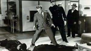 A man in a suit standing on a man lying on a man's body.
