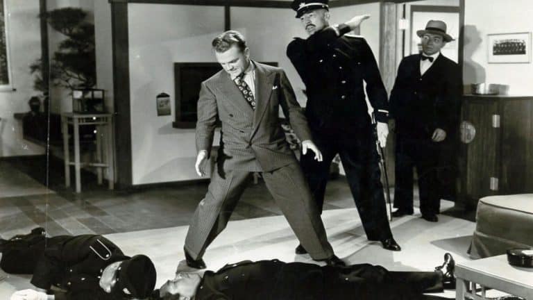 A man in a suit standing on a man lying on a man's body.