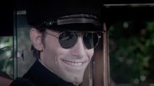 A man in a black hat and sunglasses is smiling.