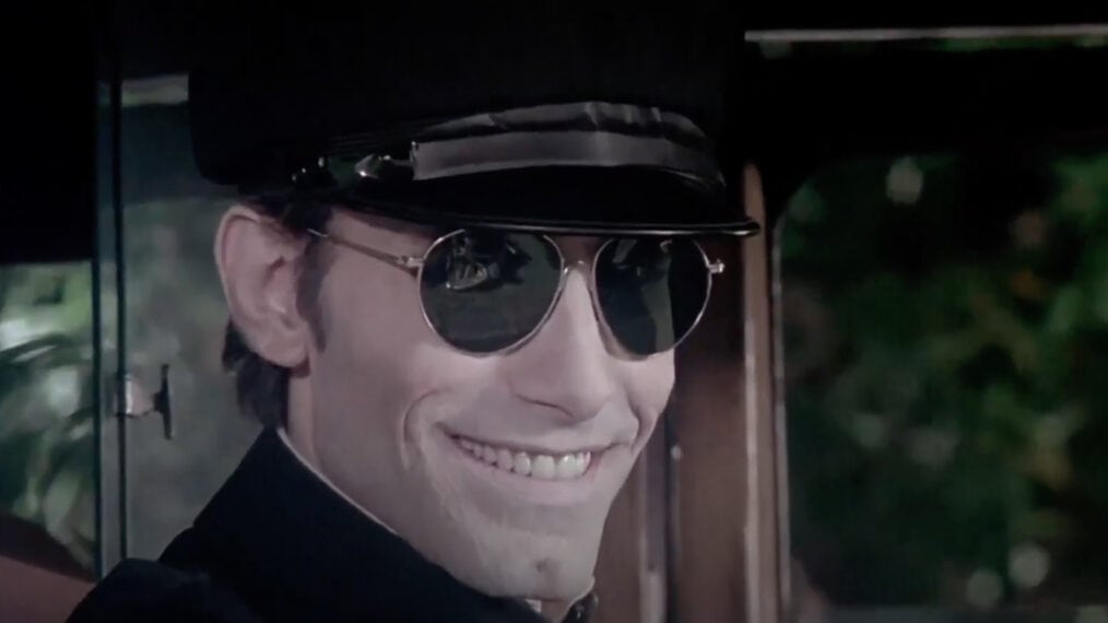 A man in a black hat and sunglasses is smiling.
