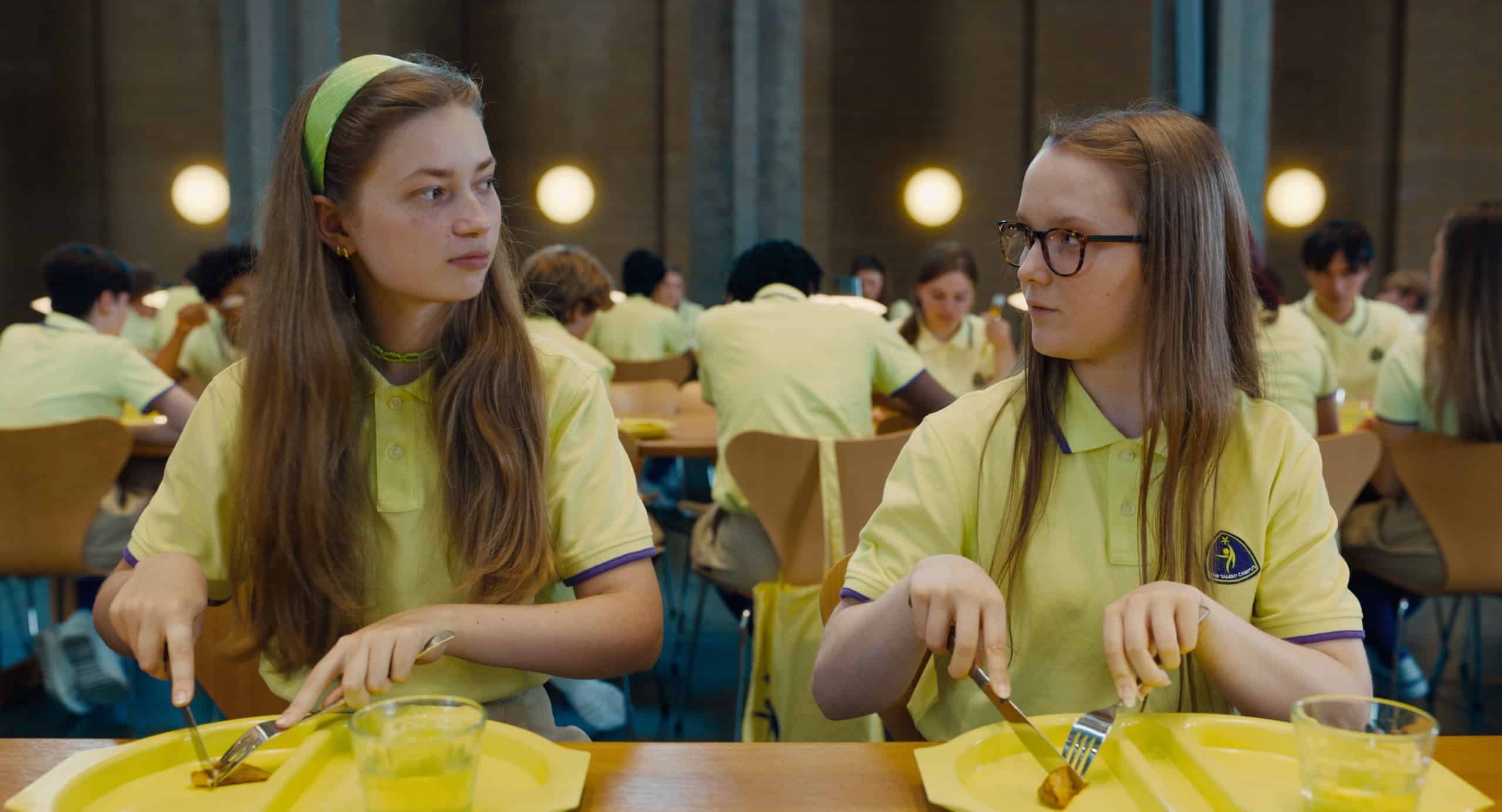Two students in yellow uniforms sitting at a cafeteria table.