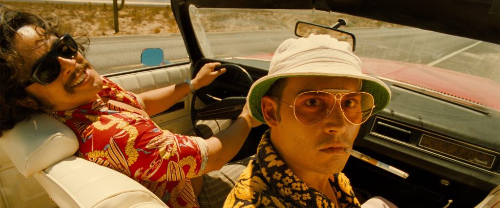 Two individuals enjoying a ride in a vintage convertible car on a sunny day.